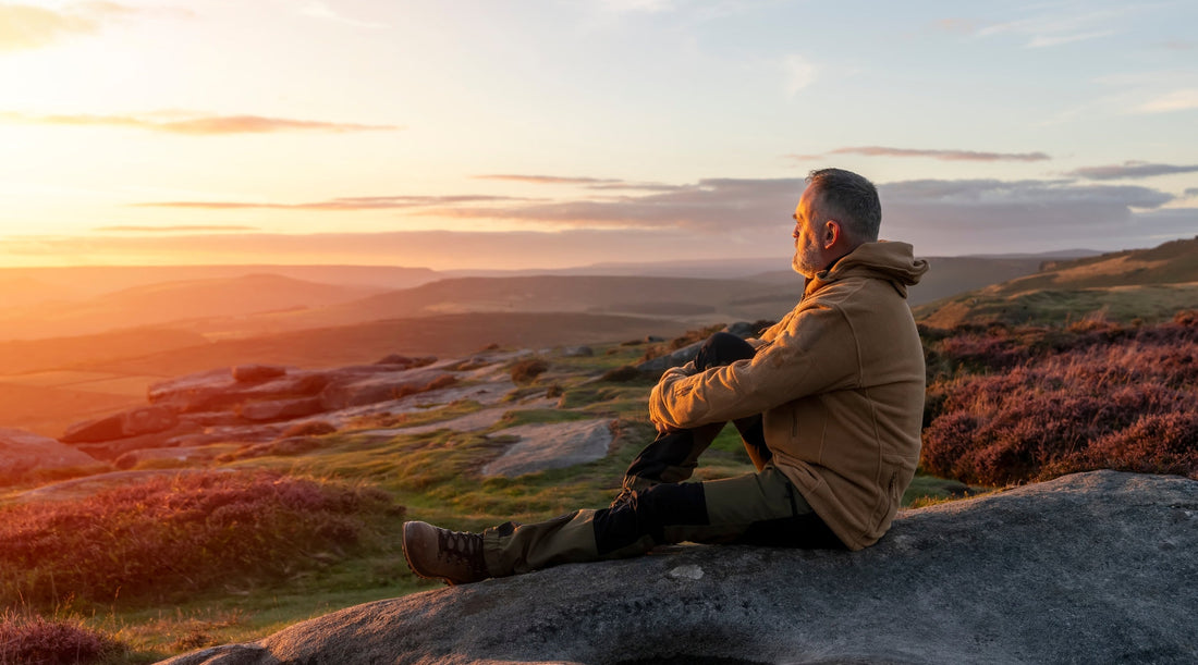 A picture of a man on a rock watching the sunset.