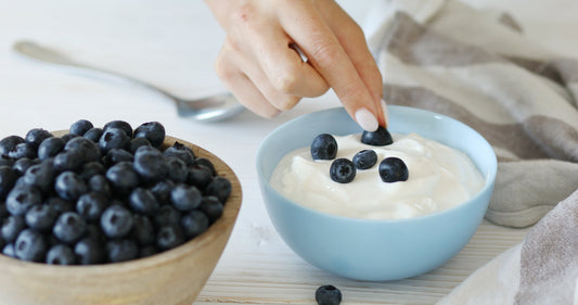 Female hands adding fresh blueberries to a bowl of yogurt.