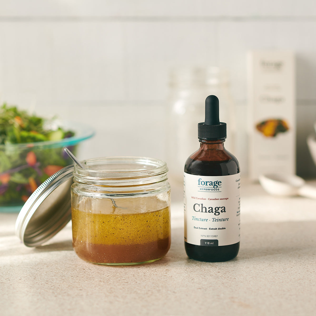 A Forage Hyperfoods Chaga tincture in the original format next to a healthy salad dressing, which the tuncture has been added to showing its everyday ease of use. Easy to apply to your day to day foods.