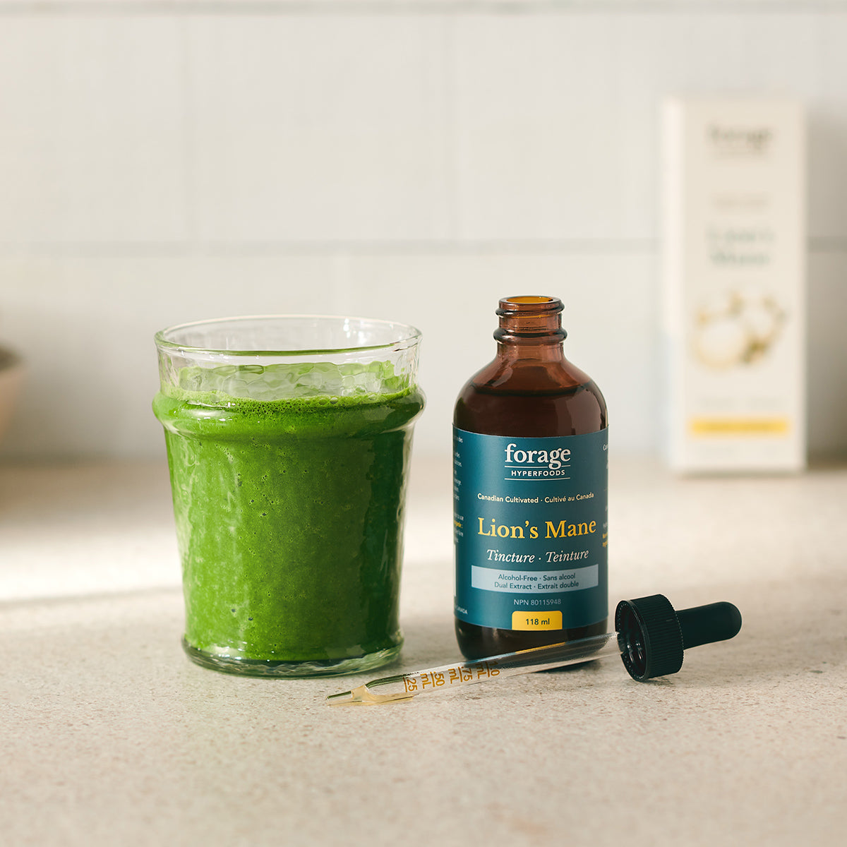 A tincture bottle of Alcohol-Free Lion's Mane Tincture from Forage Hyperfoods next to a healthy green smoothie, showing the products ease of use.
