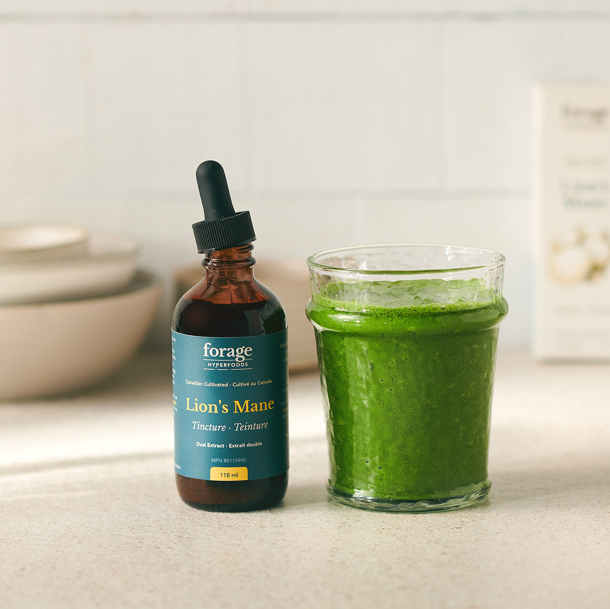 A tincture bottle of Original Lion's Mane Tincture from Forage Hyperfoods next to a healthy green smoothie, showing the products ease of use.