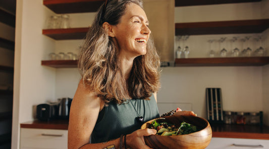 A woman holding a salad, looking into the sunlight of a window. 