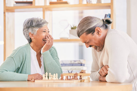 Senior couple laughing as they play chess for relaxing, bonding and spending time together at home. Marriage, retirement and happy man and woman enjoy board game for challenge, strategy and thinking.