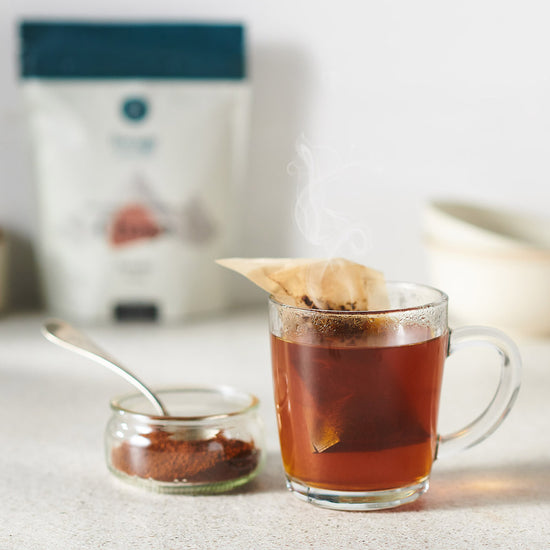 Ground Chaga powder tea in a transparent mug with a tea bag. It's warm and cinnamon coloured. 