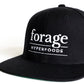 A black snapback hat with white "forage hyperfoods" embroidered on the front. There is a closeup of the text. 
