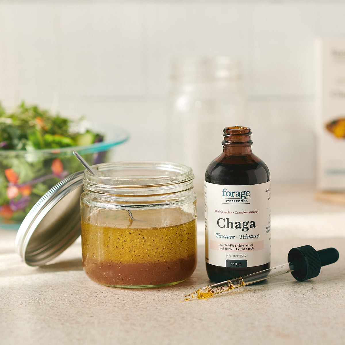 A Forage Hyperfoods Chaga tincture in the alcohol-free format next to a healthy salad dressing, which the tuncture has been added to showing its everyday ease of use. Easy to apply to your day to day foods.