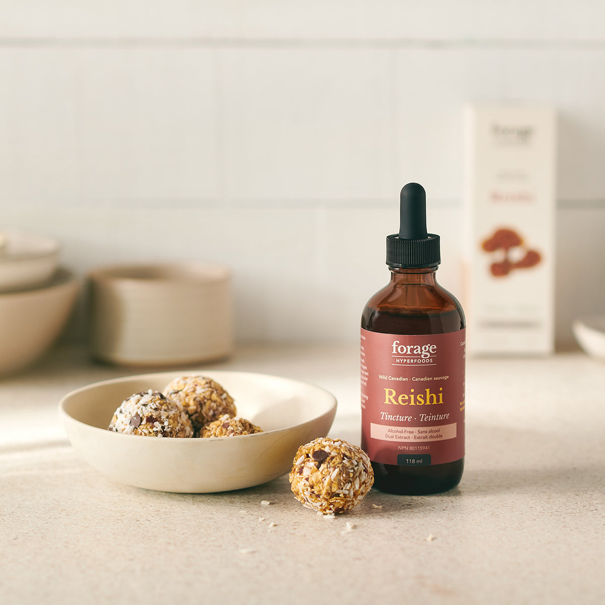 A tincture bottle of Alcohol-Free Reishi Tincture from Forage Hyperfoods next to a healthy date and nut ball showing the products ease of use