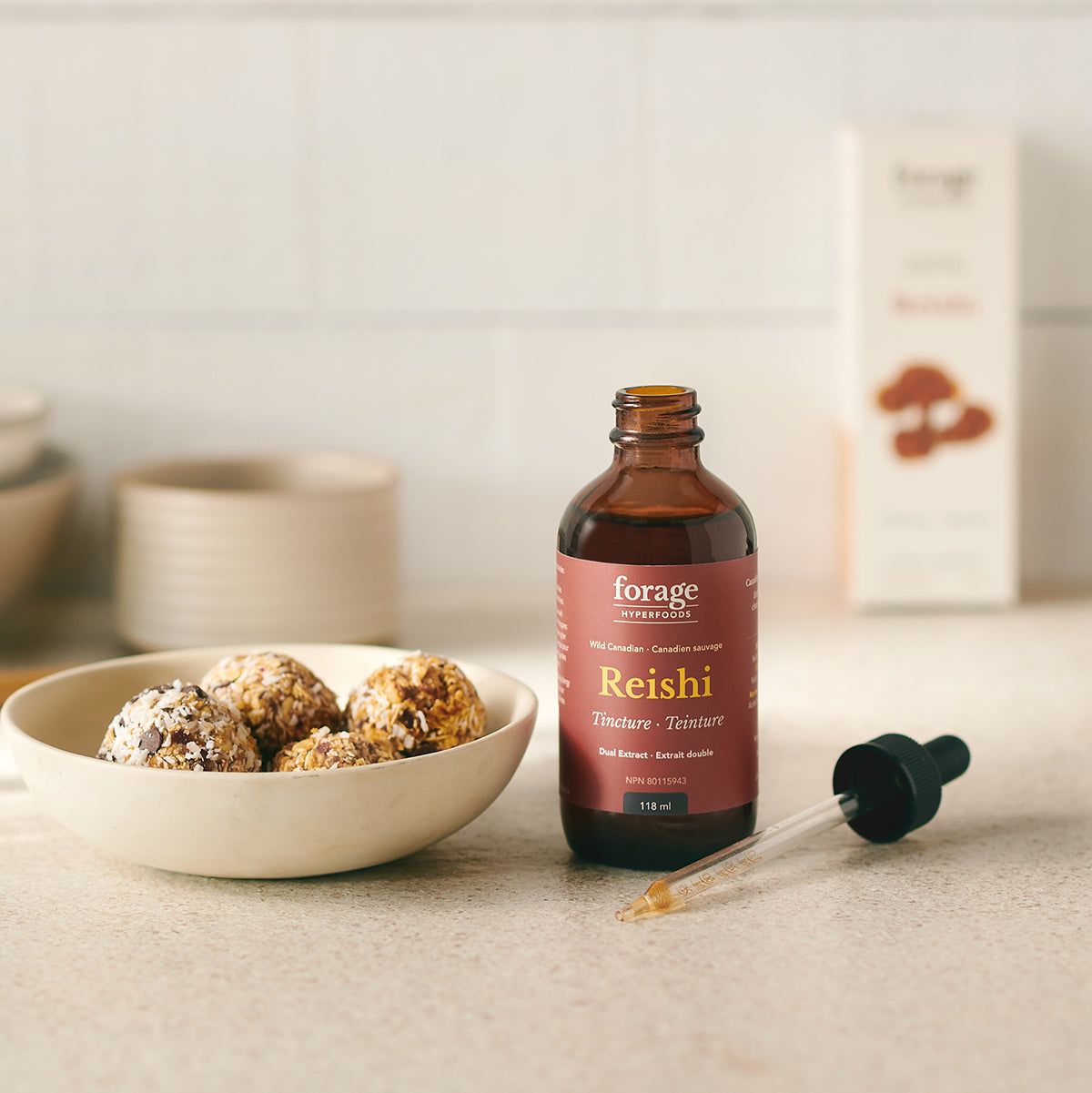 A tincture bottle of Original Reishi Tincture from Forage Hyperfoods next to a healthy date and nut ball showing the products ease of use