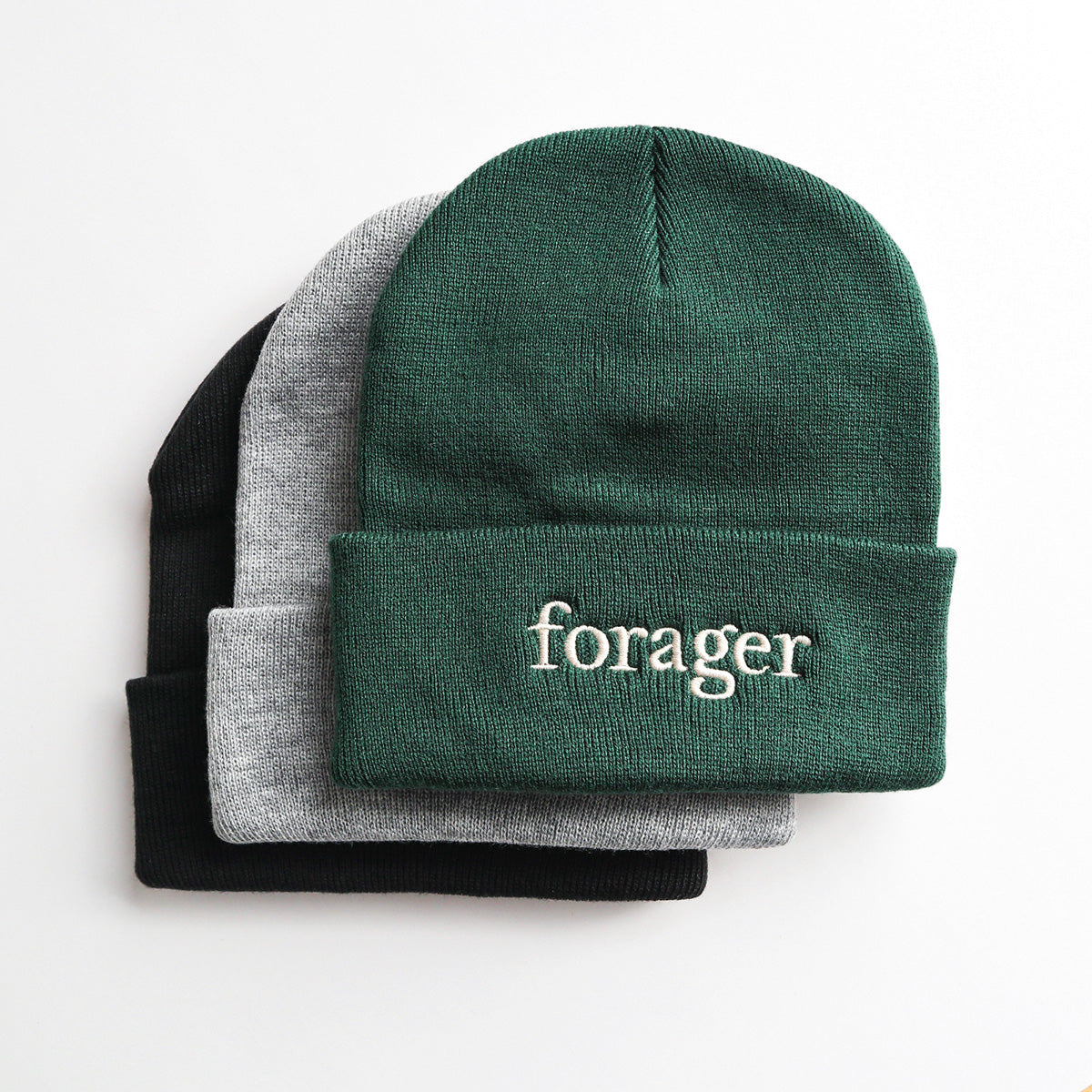 A stack of 3 beanies. The first is green, the second is gray and the last is black.