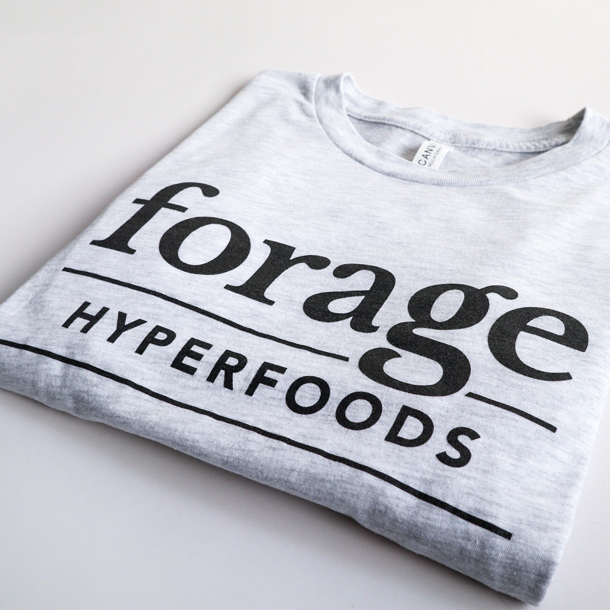  A light gray shirt with the word mark "Forage Hyperfoods" printed on it in black. It is laid out flat on a white background.  It is folded.