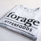  A light gray shirt with the word mark "Forage Hyperfoods" printed on it in black. It is laid out flat on a white background.  It is folded.